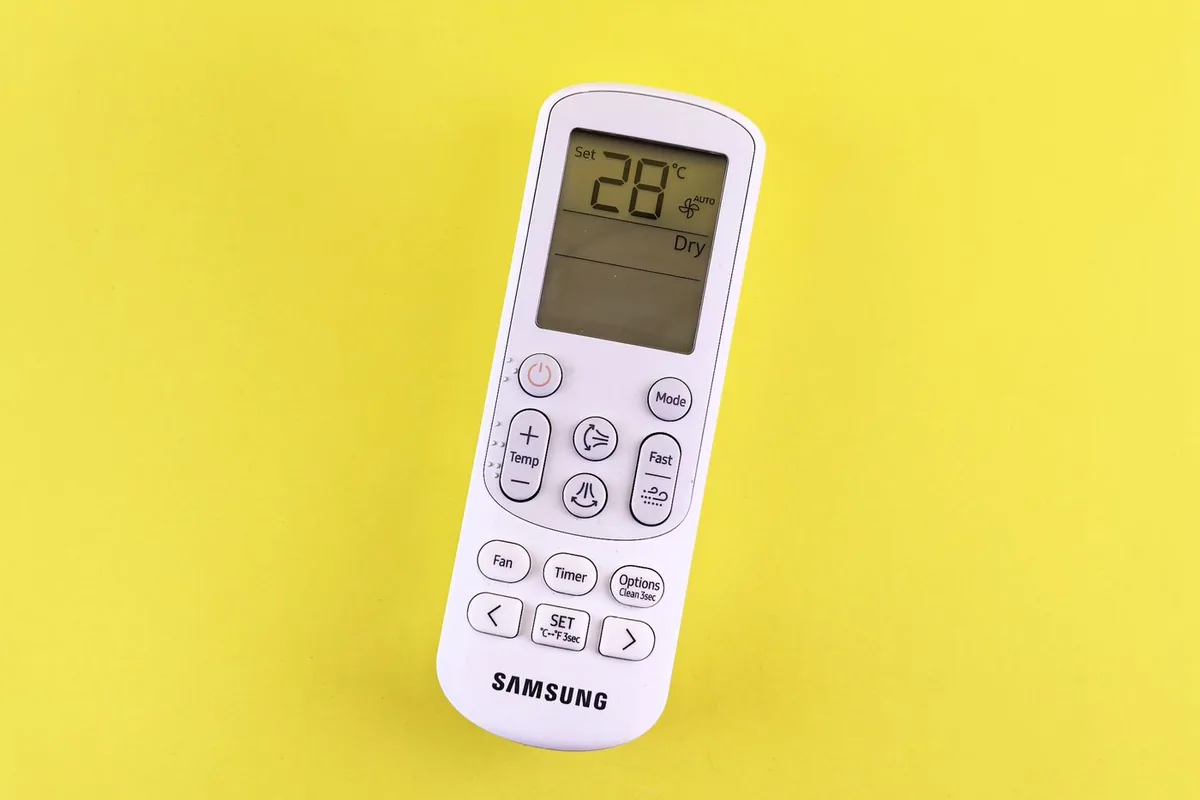 Air conditioner remote control on a yellow background showing a temperature setting